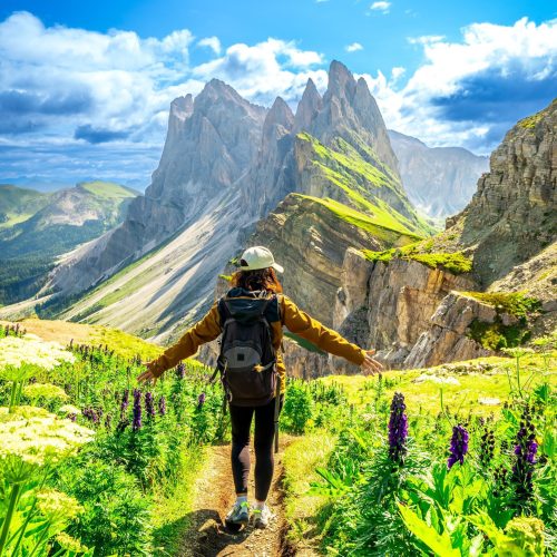 Female hiker walking on a path enjoying beautiful mountain landscape during summer hike in seceda, dolomites, italy
